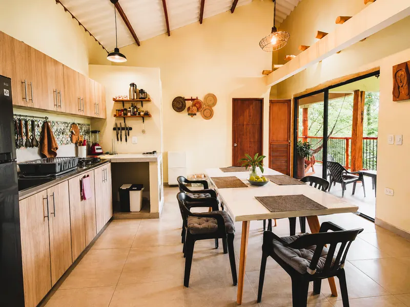 Kitchen with wooden cabinets and a dining table, with the terrace and greenery beyond