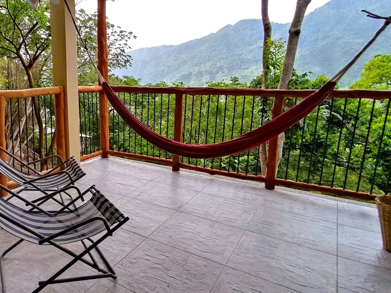 Terrace with a red hammock and two lounge chairs, looking out to forested mountains