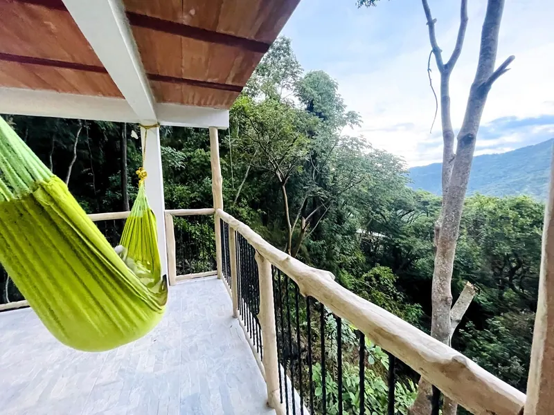 Green hammock on the covered terrace, with a wooden railing and tropical forest beyond